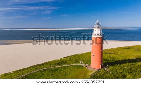 A unique perspective drone view at the lighthouse of Texel standing tall on a sandy beach, against a backdrop of the ocean waves crashing. The iconic red lighthouse of Texel Netherlands