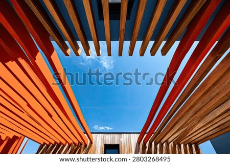 A unique perspective looking up through a modern architectural structure featuring wooden slats against a vibrant blue sky.