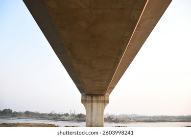 A unique perspective of the underside of a concrete bridge spanning over a calm body of water.