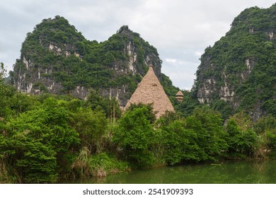 Unique pyramid-shaped thatched hut surrounded by lush greenery and limestone mountains, capturing the harmony of nature and traditional architecture. - Powered by Shutterstock