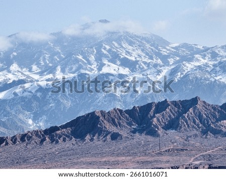 The unique red rock formations of Mars Canyon sit in the foreground with the water of Issyk Kul lake and snow covered mountains beyond