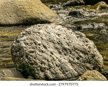 Unique rock formations eroded by water in a shallow river stream surrounded by larger boulders and natural scener