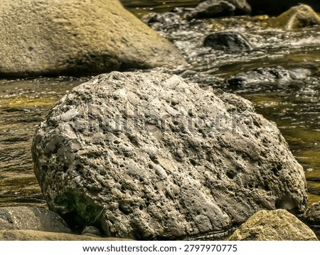 Unique rock formations eroded by water in a shallow river stream surrounded by larger boulders and natural scener