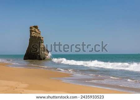A unique rock spire withstands the ocean's waves on a sandy beach. The dynamic interplay of water and erosion is a testament to nature's artistry.