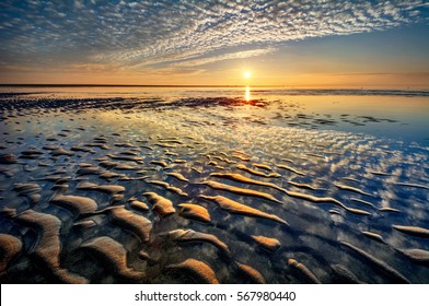 Unique sand ridges over on an ocean beach during a bright colorful sunrise and blue skies with streaky clouds