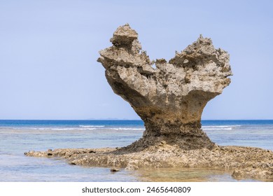 The unique shape of the rock resembles an abstract sculpture with intricate details, set against the ocean and clear blue sky. It is a serene and beautiful natural scene. - Powered by Shutterstock