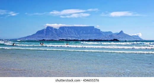 Unique Table Mountain On A Background Of Blue Sea, Mountains And Surfers In Cape Town. Beautiful South Africa. People Enjoy Vacation In Cape Town. Amazing Ocean Beach. Wonderful Seascape. Blouberg