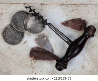 Unique Vintage Collection Of Antique Corkscrew, Native American Arrowheads, And Silver Dollar Coins On Fade Paper Background In Close Up View 