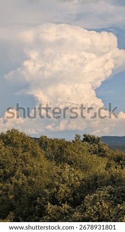 Uniquely shaped vertical cloud lingering over the green mountaintop