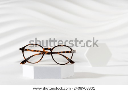 Unisex eyeglasses in a tortoiseshell plastic frame on podium on white background. Trendy eyewear minimal still life. Optic store discount, sale. Copy space. Trendy eyewear photography