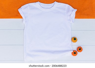 unisex kids T Shirt Mockup on a white Wooden Background with pumpkins and orange fabric. Halloween white t shirt mock up