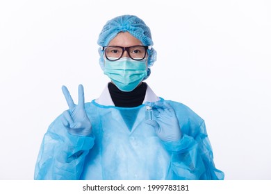 Unisex Scientist Wear Full PPE Suit, Glove, Helmet. Medical Doctor Shows Victory Okay Finger Sign With Vaccine Bottle Dose. Isolated White Background Copy Space