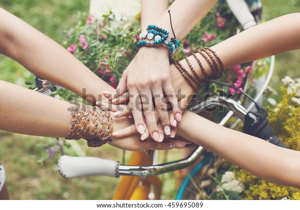 United hands of young females. Stylish hands\
of girlfriends in boho hippie bracelets near bicycle handlebar, top\
view. Togetherness and support, youth fashion and active lesiure.\
Women friendship