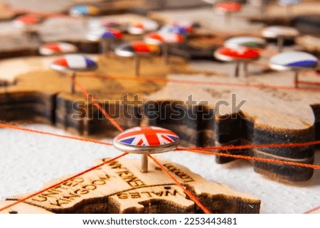United Kindom flag on the pushpin with red thread showed the paths of movement or areas of influence in the global economy on the wooden map. Planning of traveling or logistic concept. Network