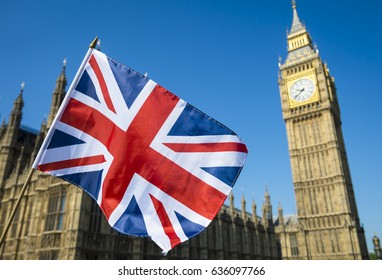 United Kingdom flag waving in bright blue sky in front of the Houses of Parliament at Westminster Palace with Big Ben