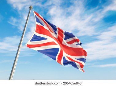 United Kingdom flag waving in the wind on flagpole. United Kingdom flag waving a blue cloudy sky