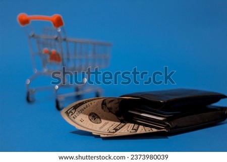 United States of America 5 and 20 dollar bills showing from black wallet  with empty shopping cart and isolated on blue background representing buying power and consumerism.