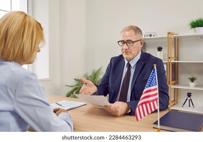United States of America Consulate embassy worker gives visa application form to lady traveling to USA. Citizenship and Immigration Services agency department officer talking to woman about her status - Shutterstock ID 2284463293