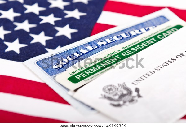 United States of America social security and green\
card with US flag on the background. Immigration concept. Closeup\
with shallow depth of\
field.