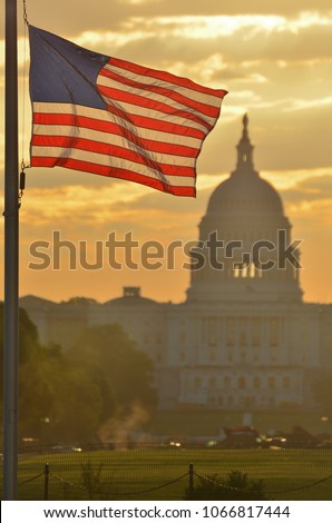 United States Capitol dome silhouette and the national flags of U.S.  rounding Washington Monument during a misty sunrise - Washington D.C. United States of America