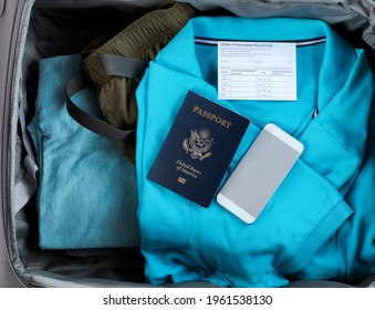 United States passport book with Covid 19 vaccination record card and smartphone inside of travel suitcase packed with clothes - Powered by Shutterstock