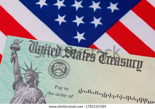 United States Treasury check and American\
flag. Concept of stimulus payment, tax refund and federal\
government grants, loans, benefits and\
assistance