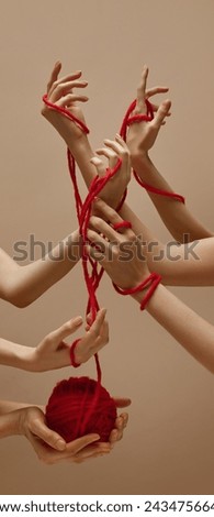 Unity. Woman's hand holds ball of red threads and other hands intertwined with each other tied with this thread against sandy color studio background. Concept of human touch, beauty and care.