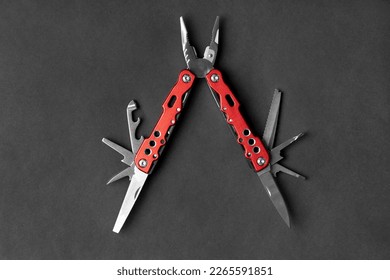 universal multifunctional knife pliers with different nozzles and a red handle on a dark gray background. Versatile camping knife. Multifunctional tool.