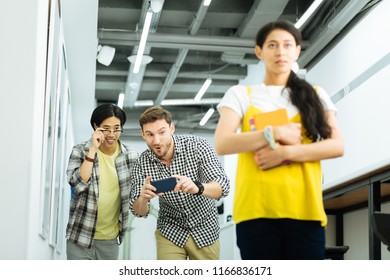 University Bullying. Nervous Ashamed Girl Walking In The University And Suffering From Two Men Taking Photos Of Her And Laughing