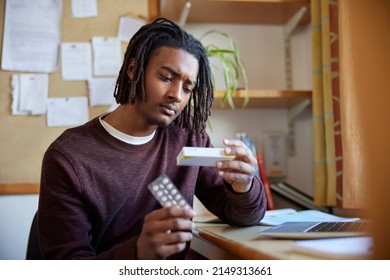 University Or College Student With Poor Mental Health Looking At Anti Depressant Medication Packaging At Desk In Room