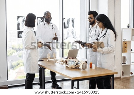 University, education, medicine, anatomy concept. Multiracial medical students with African American professor and human skeleton model in classroom, studying anatomy.