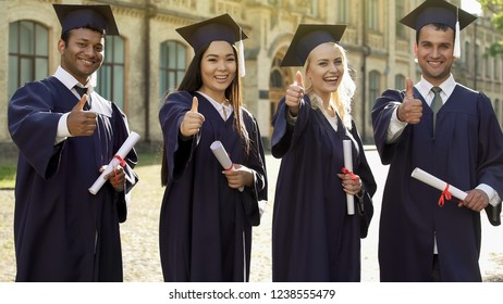 University graduates in academic regalia holding diplomas, showing thumbs-up - Shutterstock ID 1238555479