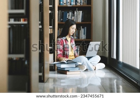 University Library: Beautiful smart asian university student uses Laptop, Writes Notes for Paper, Essay, Study for class assignment. Focused students learning, studying for college exams.