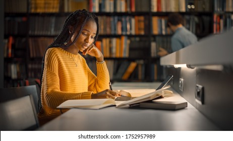 University Library: Gifted Black Girl Uses Laptop, Writes Notes For The Paper, Essay, Study For Class Assignment. Students Learning, Studying For Exams College. Side View Portrait With Bookshelves