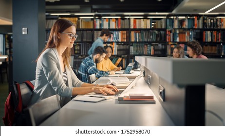 University Library: Talented Caucasian Girl Sitting At The Desk, Uses Laptop, Writes Notes For The Paper, Essay, Study For Class Assignment. Diverse Group Of Students Learning, Studying For Exams.