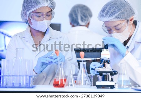 University science students learning practical chemistry experiment. Young researchers in protective uniforms studying red liquid reaction in laboratory room site. Professional biotechnology experts analyzing DNA structure on digital screens. Scientists in safety gear conducting microscopic research for medical innovation. Collaborative medical research team working together in modern science laboratory. Male and female scientists analyzing red chemical sample with microscope tool.