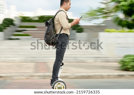 University student with backpack checking smartphone when rising on e-scooter, blurred motion