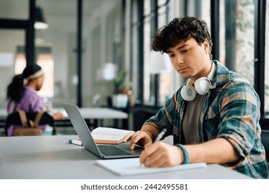 University student writing while using laptop and studying in the classroom. Copy space. 
