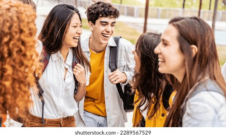 University students talking and laughing together in college campus - Happy teenagers having fun going to school - Friendship concept with guys and girls hanging out on summer day 