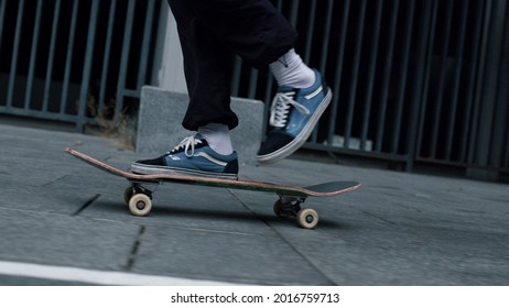 Unknown active man feet riding on skateboard outdoor. Unrecognizable sporty hipster making trick with skateboard on urban background in slow motion. Unknown skater guy jumping kickflip outside.