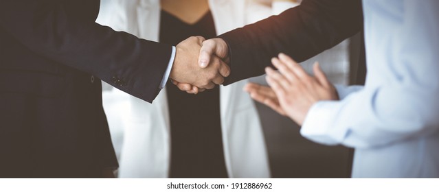 Unknown businesspeople are shaking their hands after signing a contract, while standing together in a sunny modern office, close-up. Business communication, handshake, and marketing concept - Powered by Shutterstock