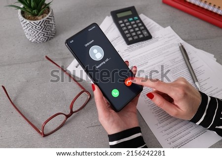 Unknown caller. A woman holds a phone in his hand and thinks to end the call. Incoming from an unknown number. Incognito or anonymous. Businesswoman can't take the call because she is at work.