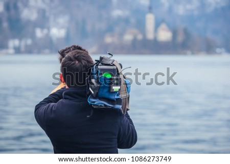 An unknown cameraman is filming a famous lake of Bled, Slovenia in a winter time. Concept of famous and beautiful places being filmed on tape.