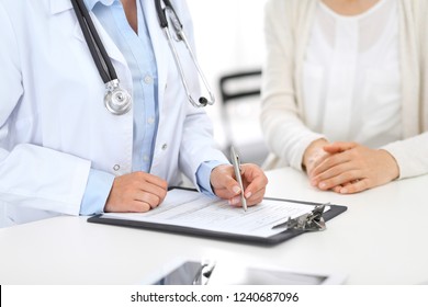 Unknown doctor and  female patient  discussing something while standing near reception desk in emergency hospital. Physician at work in clinic. Medicine and health care concept