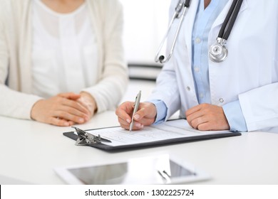 Unknown doctor and  female patient  discussing something while standing near reception desk in emergency hospital. Physician at work in clinic. Medicine and health care concept