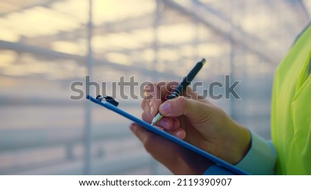 Unknown factory supervisor checking producing in greenhouse analyzing data. Closeup businesswoman hands examining glasshouse making notes inspecting production. Business inspection worker concept