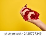 unknown female model squeezing red delicious jello in her hand on vibrant yellow background