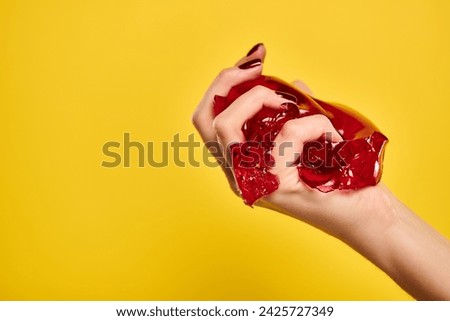 unknown female model squeezing red delicious jello in her hand on vibrant yellow background