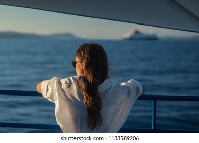 Unknown female in a white dress, long brown hair and sunglasses is enjoying the evening sun on a ferry boat. Another ferry boat is seen in the background. Travel concept. - Powered by Shutterstock