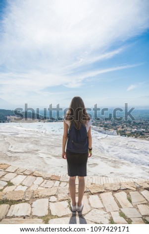 An unknown girl stands with her back standing on a rock looking at the landscape of mountains under a blue sky with light cirrus clouds on a bright sunny day. Denizli. Pamukale. Turkey